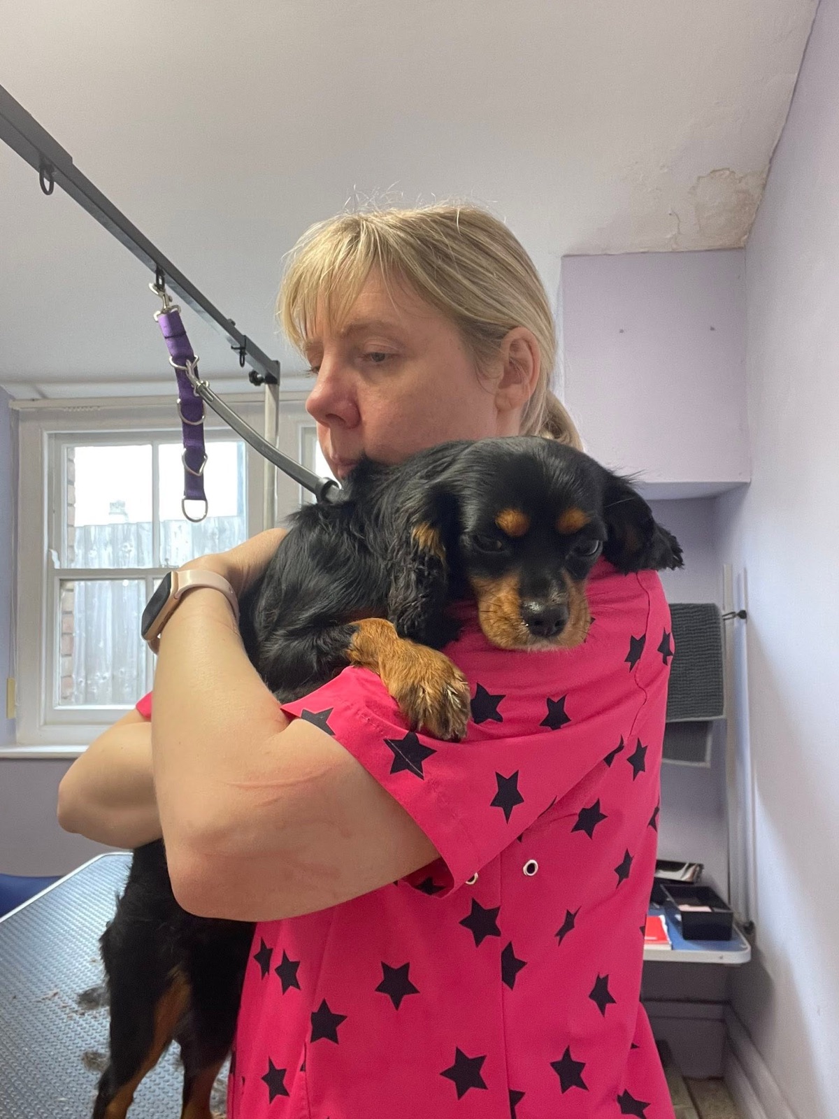 Gem, in a pink star-print grooming top, holding a puppy in the parlour.